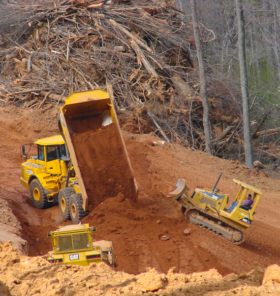Articulated trucks  and bulldozers work together to place fill and grade slopes